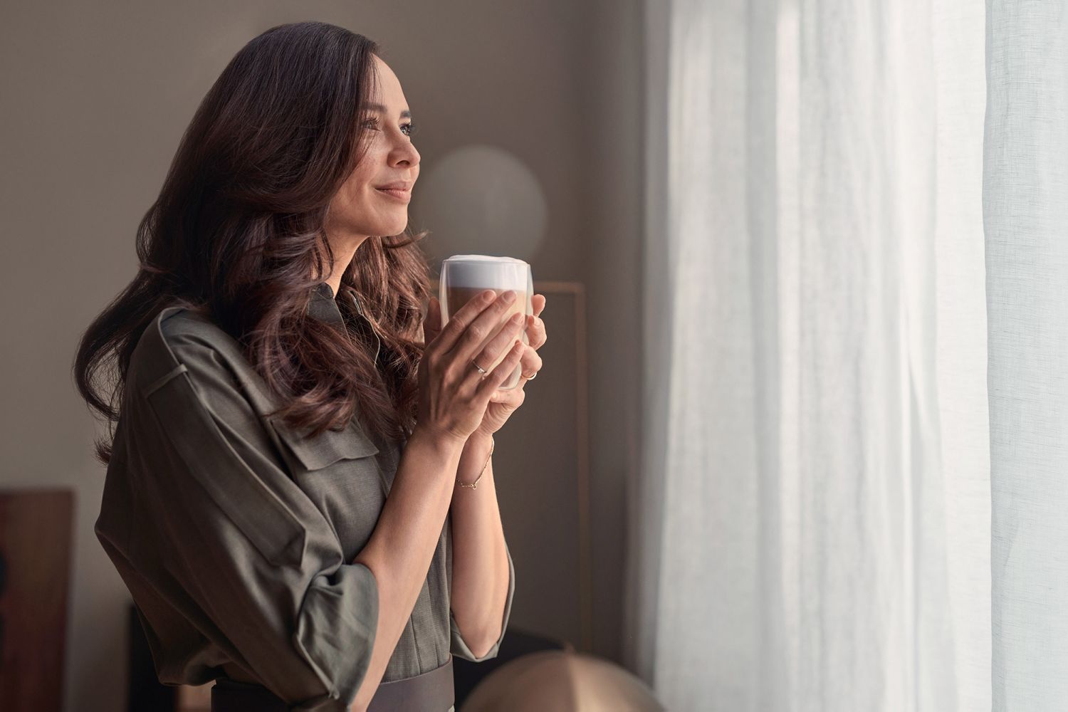 Eine Frau steht am Fenster und trinkt Kaffee